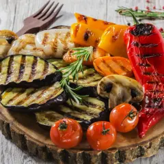 Nietypowe dania z grilla: grillowany bakłażan, papryka, pieczarki, pomidorki i czerwona papryka na drewnianej desce.