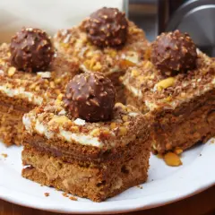 Pyszne ciasto Ferrero Rocher z kremem i orzechami, udekorowane całymi czekoladkami.