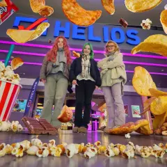 Trzy dziewczyny przed kinem Helios, otoczone przez gigantyczne przekąski. Zastanawiasz się, ile kosztuje mały popcorn w Heliosie?