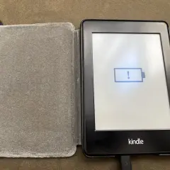 Un Kindle avec une batterie faible, prêt à être éteint. L'icône de batterie vide et le point d'exclamation indiquent qu'il est temps de le charger.