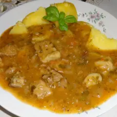 Pyszny sos do ziemniaków z kawałkami mięsa i warzyw, udekorowany listkiem bazylii.
