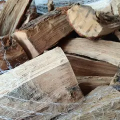 Un tas de bois sec, prêt à crépiter dans la cheminée. Les bûches sont emballées dans un filet blanc.