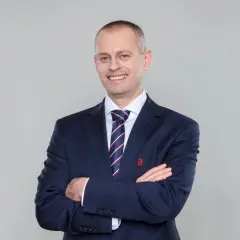 Marcin Włodarski, trener, w granatowym garniturze i krawacie, z rękami skrzyżowanymi na piersi, uśmiecha się do obiektywu.