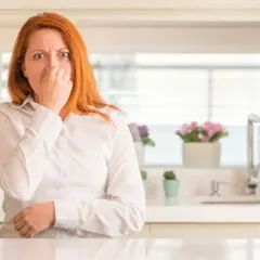 Mujer pelirroja se tapa la nariz, con cara de asco, por unos gases con olor a huevos podridos en la cocina.