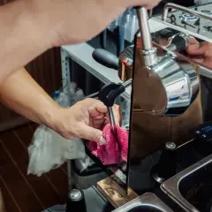 Ręce barista czyszczą dyszę ekspresu, przygotowując go do odkamieniania. Dbałość o sprzęt zapewnia idealne lattego.