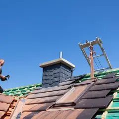 Pracownik na dachu układa dachówki, przygotowując się do prac związanych z tym, jak ocieplić komin na strychu.
