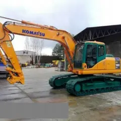 Pomarańczowa koparka gąsienicowa Komatsu PC 180 LC z zielonym podwoziem stoi na placu budowy.