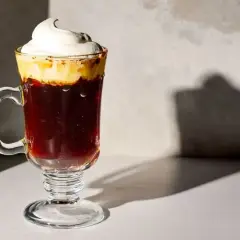 En härlig kaffedrink med vispad grädde som toppar den mörka drycken i ett glas med fot.