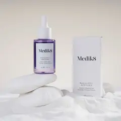 Serum Medik8 z bakuchiolem, roślinnym retinolem, na białych kamieniach i piasku.