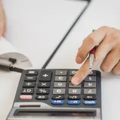 Ręka z długopisem naciska klawisz kalkulatora, licząc coś. Czy to netto?