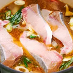 A pot of simmering Japanese fish soup with tender white fish fillets, green onions, and ginger.