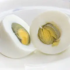 Un œuf dur vert, coupé en deux, révèle un jaune orangé entouré d'une fine couche verdâtre.