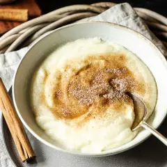 Cremiger Grießbrei mit Zimt und Zucker bestreut, ein einfaches und leckeres Grießbrei Rezept. Daneben liegen Zimtstangen.