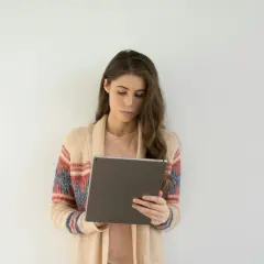 Młoda kobieta w kardiganie z wzorami przegląda tablet, szukając ofert pracy dla psychologa online.