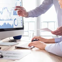 Dwóch analityków analizuje wykresy giełdowe na monitorze, dyskutując o strategii buy limit co to.