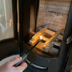 En hand tänder ved i en kamin. Det syns lite tjära i skorstenen.