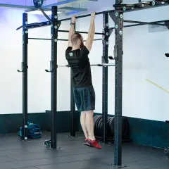 Mężczyzna wykonuje scapular pull ups na drążku. Ćwiczy plecy i ramiona w siłowni.