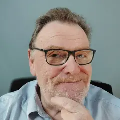 Porträt eines älteren Mannes mit Brille und Bart, der nachdenklich seinen Finger am Kinn hat.