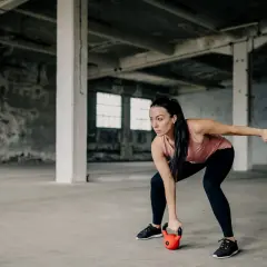 Kobieta w koszulce treningowej wykonuje ćwiczenie z kettlebell w opuszczonej hali.