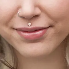 Usta z błyszczącym błyszczykiem i kwiatowym medusa piercingiem. Kolczyk w nosie dodaje uroku.