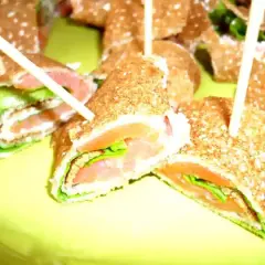 Rouleaux de galette sarrasin garnis de saumon fumé et de salade verte, servis sur une assiette jaune vif.