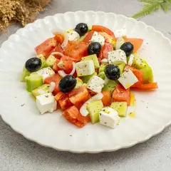 Ensalada griega fresca con tomates, pepinos, cebolla, aceitunas negras y queso feta en cubos, aderezada con aceite de oliva y hierbas.