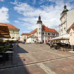 Rynek w Mariborze z kawiarnianymi ogródkami i zabytkowymi budynkami.