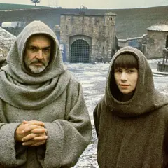 William i Adso z "Imienia róży" w klasztornych habitach, na tle kamiennych budowli i zaśnieżonego dziedzińca.