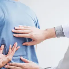 Dłoń terapeuty bada plecy pacjenta, szukając oznak bólu. Może to być wstęp do terapii, ale warto pamiętać o potencjalnych skutkach ubocznych nastawiania kręgosłupa.
