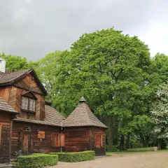Drewniany dworek w Ożarowie koło Wielunia, otoczony bujną zielenią.