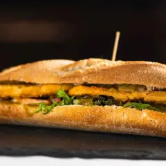 Un bocadillo caliente con rebozado crujiente, lechuga fresca y pepinillos, servido en pan rústico.