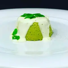 Sformato di pecorino verde brillante, ricoperto da una salsa bianca cremosa e guarnito con foglie verdi fresche.