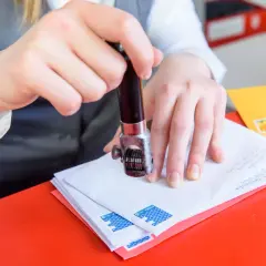 Ręce stemplują koperty. Na jednej z nich widać znaczek pocztowy z motywem fal.