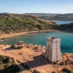 Kamienna wieża strażnicza nad zatoką z piaszczystą plażą, przypominającą widok z Bugibba Beach.