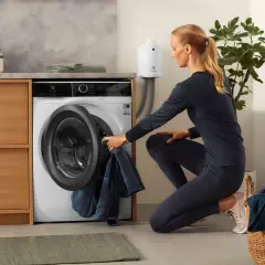 Femme chargeant du linge dans une machine, dont un vêtement en matière PBT, dans une buanderie moderne.