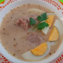 Pyszny żurek na rosole z kiełbasą i jajkiem, udekorowany natką pietruszki.