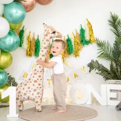 Uśmiechnięty chłopiec świętuje swój roczek, przytulając pluszową żyrafę. W tle balony i dekoracje.