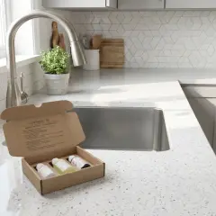 Kit de test pour mesurer le pH de l'eau dure. Trois flacons sont dans une boîte ouverte sur un comptoir de cuisine.