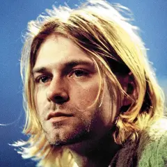 Kurt Cobain, ikona zespołu Nirvana, z charakterystycznymi blond włosami i niebieskimi oczami, na tle niebieskiego tła.