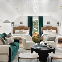 Two beds flank a window with teal curtains. Multiple rugs define the seating and sleeping areas in this cozy room.