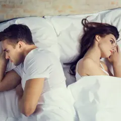Coppia a letto, schiena contro schiena, pensierosi. A volte si può stare insieme senza fare l'amore, ma la distanza emotiva è palpabile.