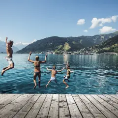 Familj hoppar i vattnet en solig zell am see sommar. Berg och stad i bakgrunden.