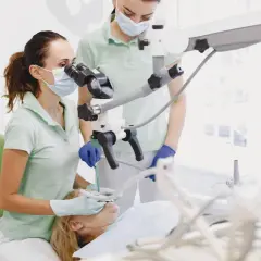 Dentystka z asystentką przy mikroskopie stomatologicznym, przygotowujące się do zabiegu, być może wyrywania ósemki.