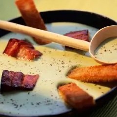 Une cuillère en bois sert une soupe de pois cassés onctueuse, garnie de lard croustillant et de croûtons dorés.