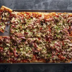 Prostokątna pizza z szynką, pieczarkami i oliwkami. Idealna inspiracja, jak zrobić pizzę na rodzinny obiad.