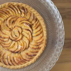Un magnifique appareil tarte aux pommes, aux pommes caramélisées disposées en spirale sur une pâte dorée, sur un plat en verre décoré.