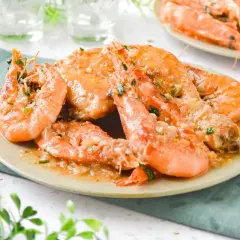 Plato de pollo con gambas en salsa de ajo y perejil, servido en un plato beige con un tenedor a la izquierda.
