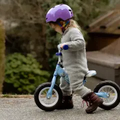 Mała dziewczynka w fioletowym kasku uczy się jeździć na rowerku biegowym. Od jakiego wieku można zacząć? Od około 18 miesięcy, gdy dziecko pewnie chodzi.