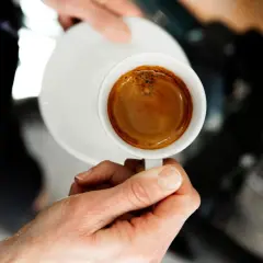 En hand håller en kopp med en perfekt dubbel espresso, med gyllene crema som lovar en intensiv smakupplevelse.