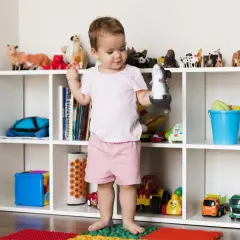 Dziecko bawi się zabawkami, a regał pokazuje, jak przechowywać pluszaki i inne zabawki, tworząc porządek w pokoju.